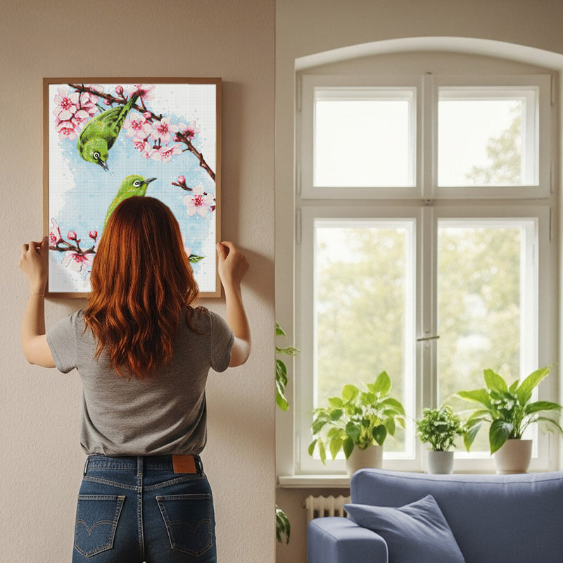 Frau hängt Diamond Painting mit grünen Vögeln und Blumen an der Wand auf