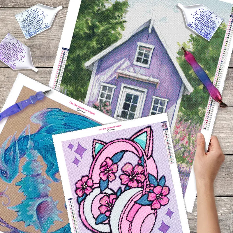 Drei Diamond Painting Bilder mit funkelnden Steinchen und Zubehör auf dem Tisch
